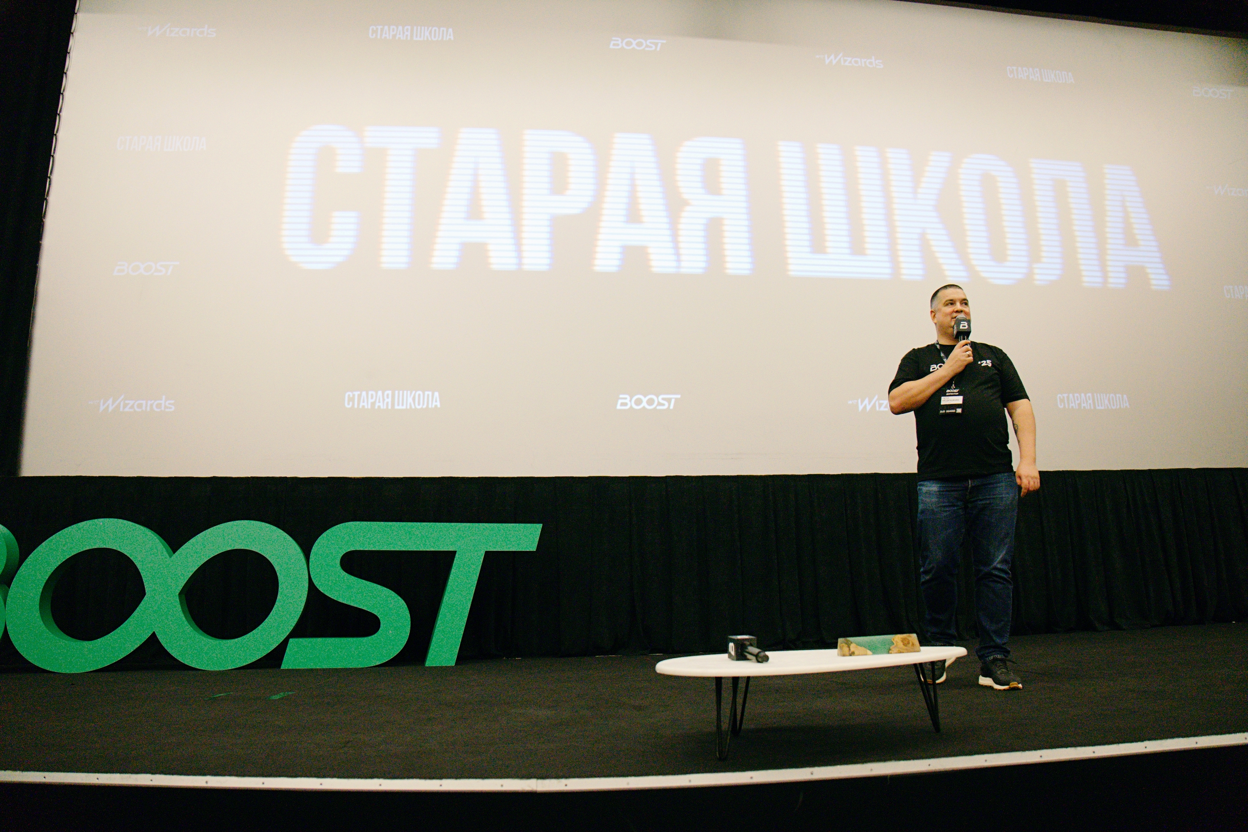 [PERSON_1] на сцене конференции BOOST на фоне экрана «Старая школа»